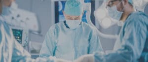A surgeon in blue scrubs and mask working on something.