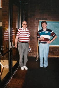 Two men standing next to each other in front of a brick wall.