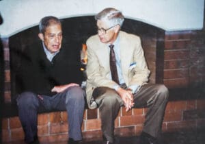 Two men sitting on a brick wall talking.