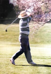 A man in striped shirt swinging at golf ball.