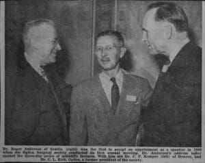 Three men are talking to each other in a room.