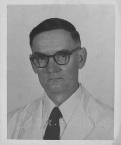 A man in glasses and a tie is wearing a white shirt.