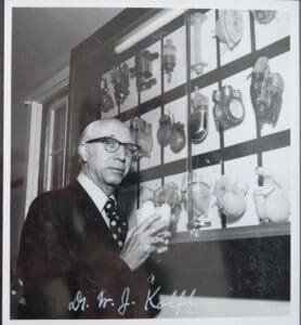 A man standing in front of a wall with many pots on it.